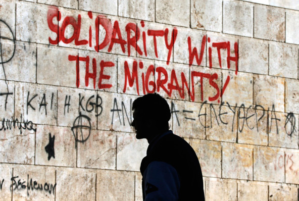 A man walks past graffiti on a wall in early December that reads "Solidarity with the Migrants" in central Athens, Greece. Dioceses and parishes participating in National Migration Week, Jan. 6-12 are asking people to work toward a comprehensive immigrat ion reform law. (CNS photo/Yannis Behrakis, Reuters)