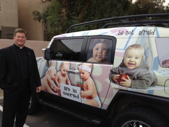 Fr. Don Kline, pastor at St. Joan of Arc, shows off his new car wrap. It offers pregnant women a resource and a direct line to help at www.gotbaby.org (courtesy photo)