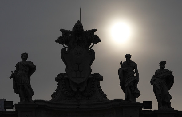 A papal tiara and keys are silhouetted between saints on the colonnade as the sun shines from behind clouds in the morning in St. Peter's Square at the Vatican March 1. Following Pope Benedict XVI's Feb. 28 resignation, the church has entered a period kn own as the interregnum. (CNS/Paul Haring)