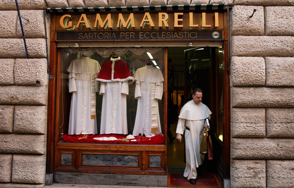 Three sizes of cassocks for the future pope are displayed in the window of the Gammarelli clerical tailor shop in Rome March 4. At the request of the Vatican the famous shop has prepared three sizes of clerical wear to be used by the new pope immediately after his election. Pictured leaving the store is Dominican Father Thomas Petri, assistant professor of theology at Providence College in Rhode Island. (CNS photo/Paul Haring) 