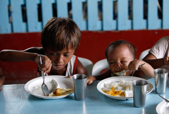 A boy and his younger brother eat their free meals May 22 during a feeding program at a slum area in Manila, Philippines. Archbishop Francis A. Chullikatt, permanent observer of the Holy See to the United Nations, told a U.N. General Assembly meeting May 23 that it was urgent to resolve the "ongoing scandal" of hunger in today's world. (CNS photo/Romeo Ranoco, Reuters) 