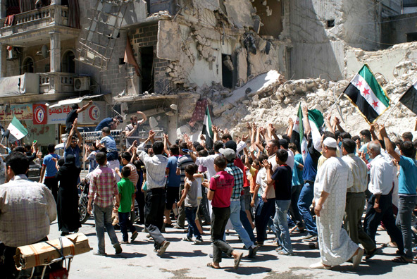 Civilians and Free Syrian Army fighters carry Syrian opposition flags and chant slogans as they walk past damaged buildings during a protest against Syria's President Bashar al-Assad in Aleppo June 14. (CNS photo/Jalal al-Halabi, Shaam News Network hando ut via Reuters)