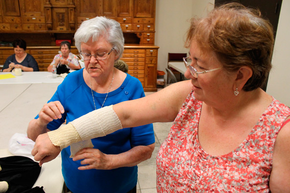 Margaret Hooks demonstrates how the bandages are used with Deb Jones, stewardship director of St. Joan of Arc Parish. (J.D. Long-Garcia/CATHOLIC SUN)