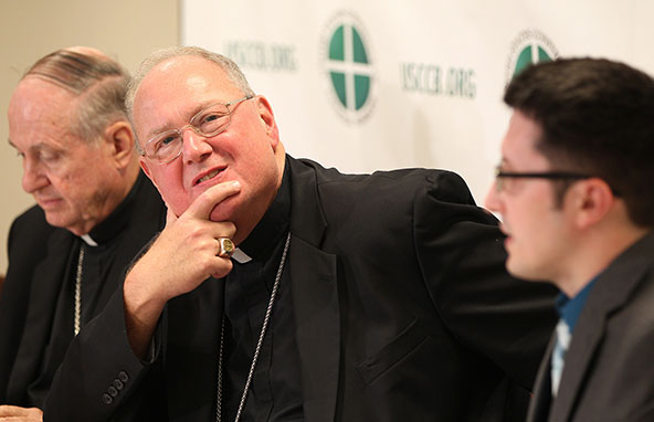 New York Cardinal Timothy M. Dolan listens to a question during a Sept. 11 press conference at the U.S. Conference of Catholic Bishops' headquarters in Washington. Also pictured is Bishop Richard E. Pates of Des Moines, Iowa, and Don Clemmer, USCCB assis tant director of media relations. Cardinal Dolan, USCCB president, and other bishops discussed the latest developments in Syria's civil war, updated their work to fight the contraceptive mandate of the Affordable Care Act and addressed attacks on the work of Catholic Relief Services worldwide. (CNS photo /Bob Roller)
