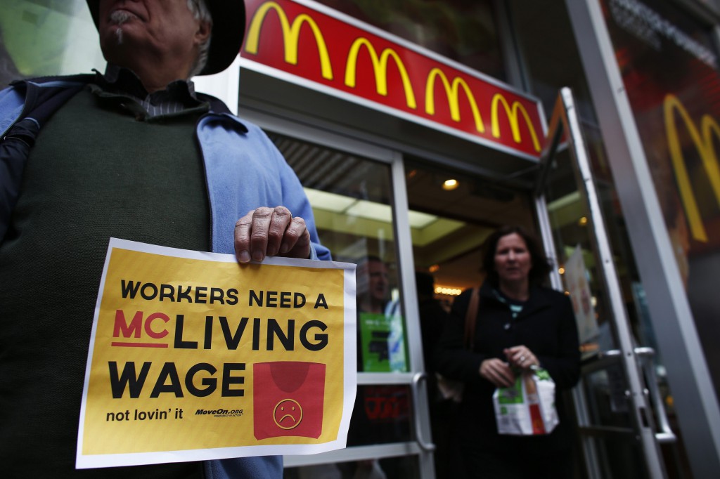 A woman exits a McDonald's restaurant in New York Dec. 4 while members of the MoveOn organization shout slogans against the company in front of the restaurant. Fast-food workers staged strikes in about a hundred U.S. cities, most of which were Dec. 5, and held rallies in other places to demand higher wages. (CNS photo/Eduardo Munoz, Reuters)