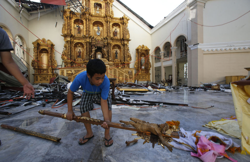 An altar server lifts up a broken crucifix as he and others clear debris from the altar area of the partially destroyed Metropolitan Cathedral in Palo, Phillippines, Nov. 15 in the aftermath of Super Typhoon Haiyan. The cathedral is one of many Catholic churches, schools and convents damaged or destroyed in the powerful storm. (CNS photo/Wolfgang Rattay, Reuters) 