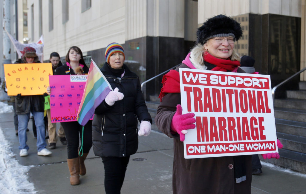 A woman carries a sign opposed to same-sex marriage while people in support of it walk behind her outside the Federal Court House in Detroit where plaintiffs April Deboer and her partner, Jayne Rowse, listened to closing arguments in their March 7 trial. A ruling in the couple's lawsuit could overturn Michigan's ban on same-sex marriage. (CNS photo/Rebecca Cook, Reuters)