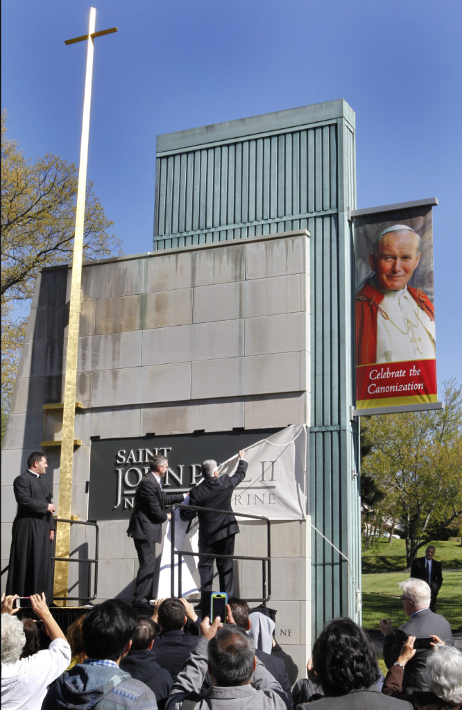 Father Gregory Gresko, left, chaplain of St. John Paul II National Shrine, joins shrine Executive Director Patrick Kelly, center, and Logan T. Ludwig, deputy knight of the Knights of Columbus, on the podium April 27 as the three men officially unveil the shrine's new name. The Washington shrine was previously named the Blessed John Paul II National Shrine, but was rededicated April 27, the day the late pope was canonized. (CNS photo/Chaz Muth)