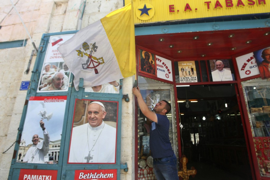 A Palestinian youth hangs a flag next to posters depicting Pope Francis outside a souvenir shop in Bethlehem, West Bank, May 19. Pope Francis will visit Jordan, the Palestinian territories and Israel during his May 24-26 Holy Land trip, his first as pope to the region. (CNS photo/Mussa Qawasma, Reuters)
