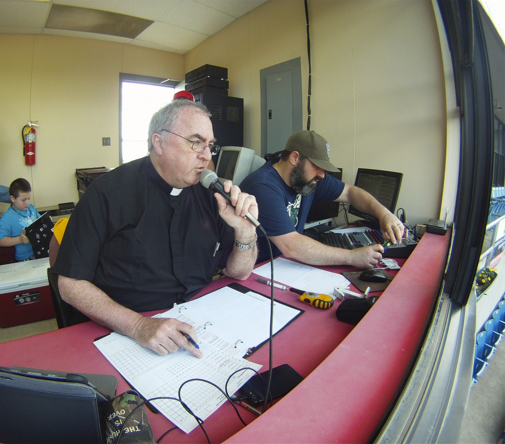 Fr. Craig Collison, a priest in the Diocese of Sioux City, Iowa, reads off his list of players as he introduces the Sioux City Explorers baseball team members in their game against the Gary, Ind., Southshore Railcats from the press box June 4. Fr. Collison, a play-by-play announcer for the minor league team, loves baseball and says being at the ballpark in a priest's collar gives him an opportunity to evangelize. (CNS photo/Jerry L. Mennenga, Catholic Globe)