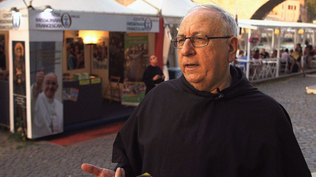 Conventual Franciscan Father Paolo Fiasconaro talks with Catholic News Service in Rome Aug. 15. Father Fiasconaro runs a missionary stand among bars and restaurants at a summer festival along the banks of the Tiber River. (CNS frame grab) 
