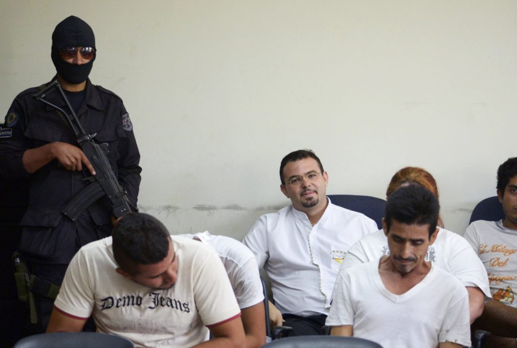 An armed guard stands near Spanish Father Antonio Rodriguez, center, during a court hearing in San Salvador Aug. 5. A Salvadoran judge ordered Fr. Rodriguez, known for his work in rehabilitating gang members, to remain in detention. He is accused of assisting gangs with criminal activities but denies the charges. (CNS photo/Jessica Orellana, Reuters)