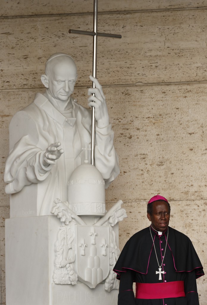 A bishop poses near a statue of Pope Paul VI outside the Paul VI hall during the morning session of the extraordinary Synod of Bishops on the family at the Vatican Oct. 16. Pope Paul will be beatified by Pope Francis Oct. 19 during the closing Mass of the synod. (CNS photo/Paul Haring)