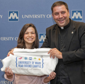 University of Mary President Monsignor James Shea gives a Year-Round Campus sweatshirt to Zoe Randazzo, an excited perspective student from St. Mary's Central High School, who was in attendance at today's press conference. Monsignor Shea announced the university's new Year-Round Campus in front of a couple hundred people that included media, students, faculty, administration and staff. 