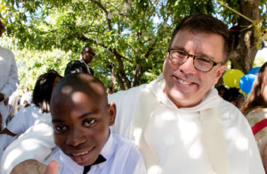 Patrick, a resident of Zanmi Beni (Haitian Creole for Blessed Friends), a home for 64 children abandoned or orphaned during the 2010 Haitian earthquake, sits with Dominican Father Charles Latou, awaiting his Dec. 21 baptism. Father Latour was one of seven Dominican priests who traveled to Haiti to baptize the children that day. (CNS photo/ Donis Tracy) 