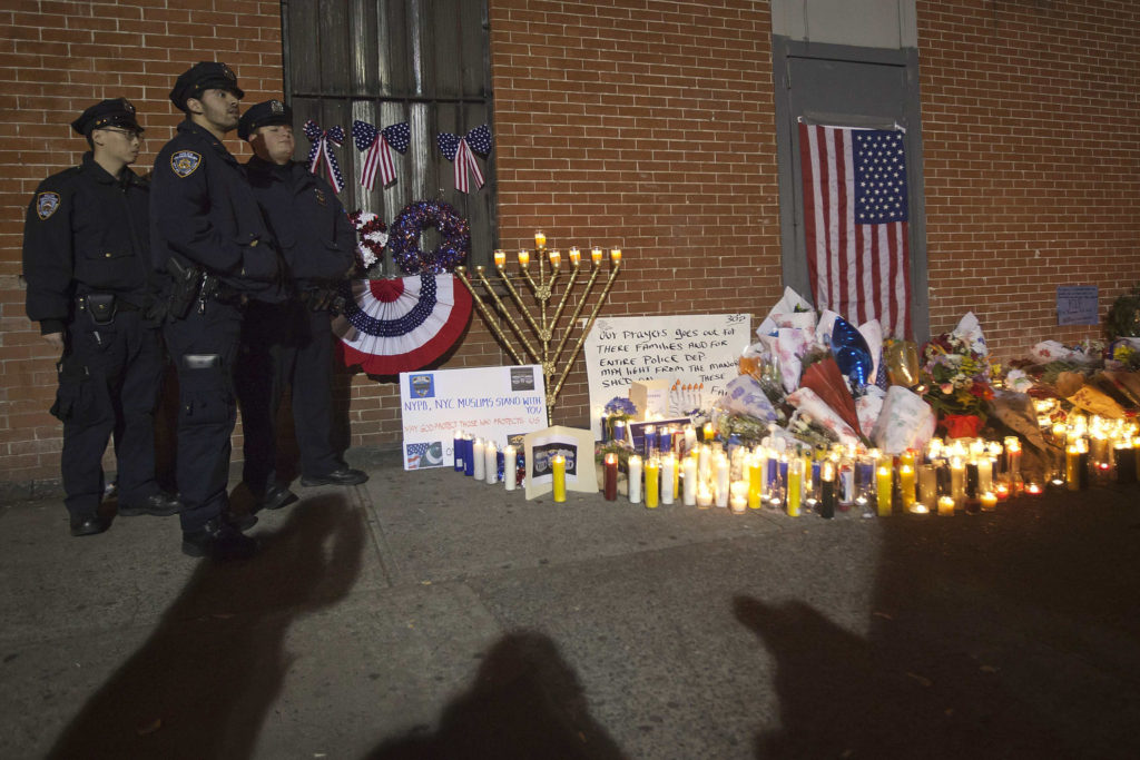 Police officers stand solemnly by a makeshift memorial solemn during a late night vigil Dec. 22 at the site where two police officers were shot in the head in the Brooklyn borough of New York. An armed man walked up to two New York Police Department officers sitting inside a patrol car and opened fire Dec. 20, shooting both of them fatally before running into a nearby subway station and committing suicide, police said. (CNS photo/Carlo Allegri, Reuters) 