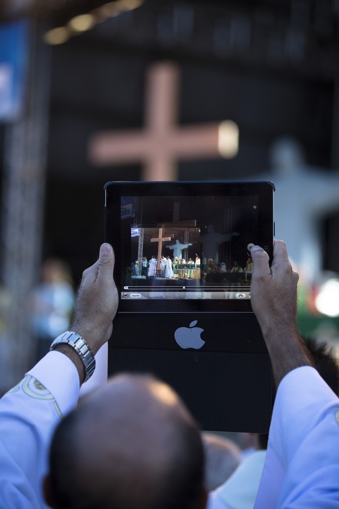 A priest records a video using his iPad during a Mass at the close of World Youth Day 2013's missionary week in Nilopolis, Brazil. (CNS photo/Tyler Orsburn)
