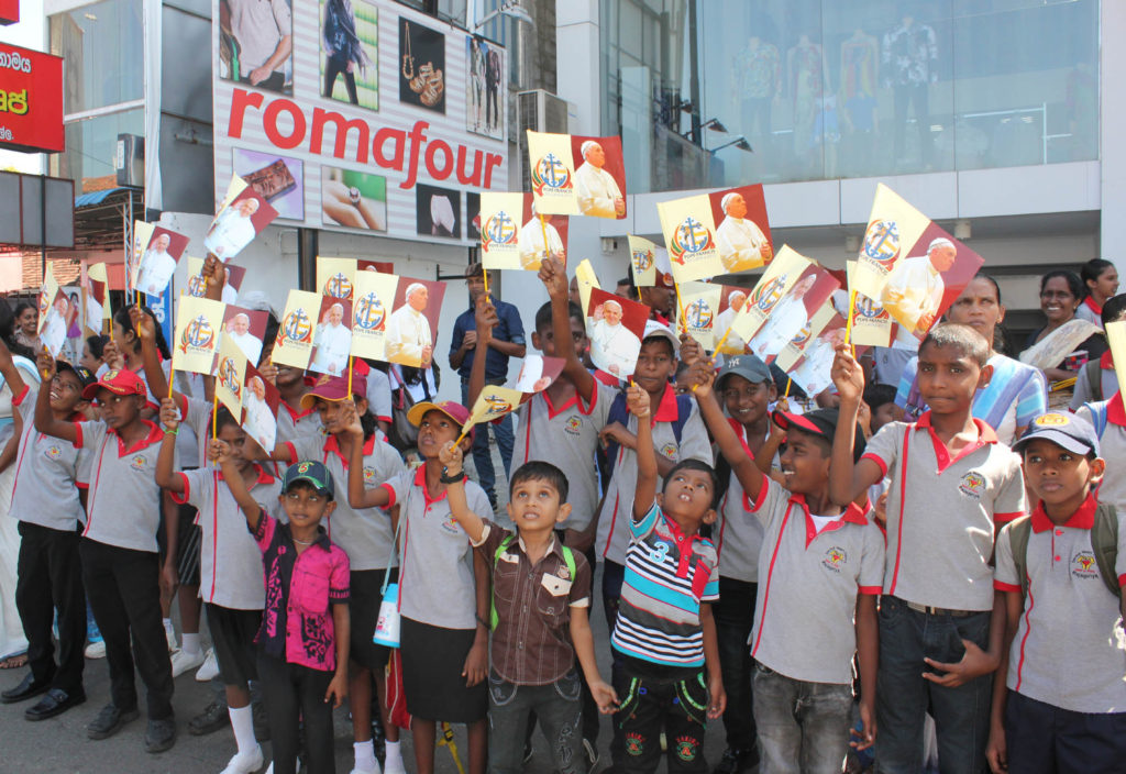 Young people wave flags as they wait for the arrival of Pope Francis in Colombo, Sri Lanka, Jan. 13. The pontiff got a rousing welcome from thousands of people lining the 17-mile route from the airport to the nunciature. (CNS photo/Anto Akkara)