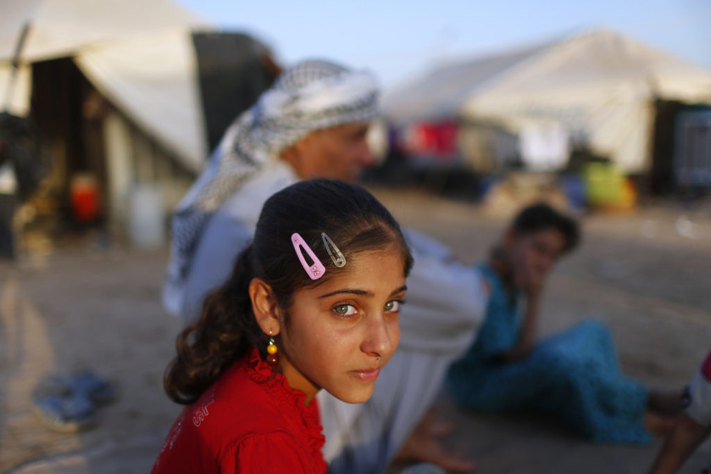 A displaced Iraqi child, who fled from violence by Islamic State militants in Mosul, sits with her family outside their tent at a camp in Irbil Sept. 14. A Jan. 25 concert at Our Lady of Mount Carmel Parish in Tempe will benefit the thousands of Catholics who fled ISIS and are living now in norther Iraq.    