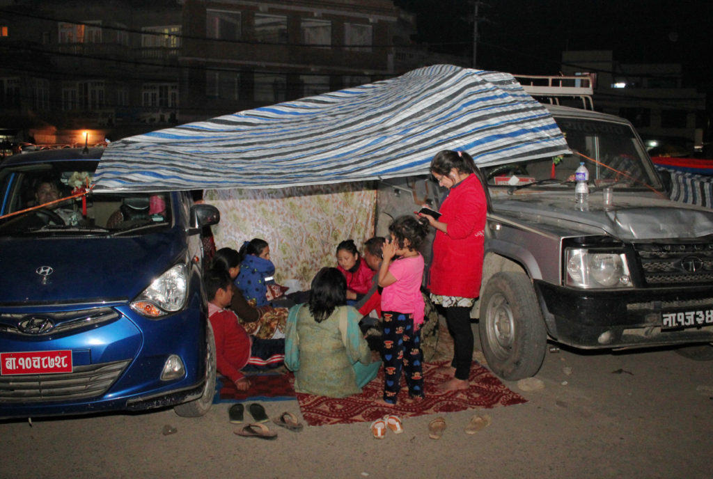 Fearing incessant tremors, families shelter themselves on a road with a plastic sheet as roof between vehicles in Kathmandu, Nepal, April 27. Inclement weather and logistical pressures have slowed down relief for Nepal earthquake victims. (CNS photo/Anto Akkara) 