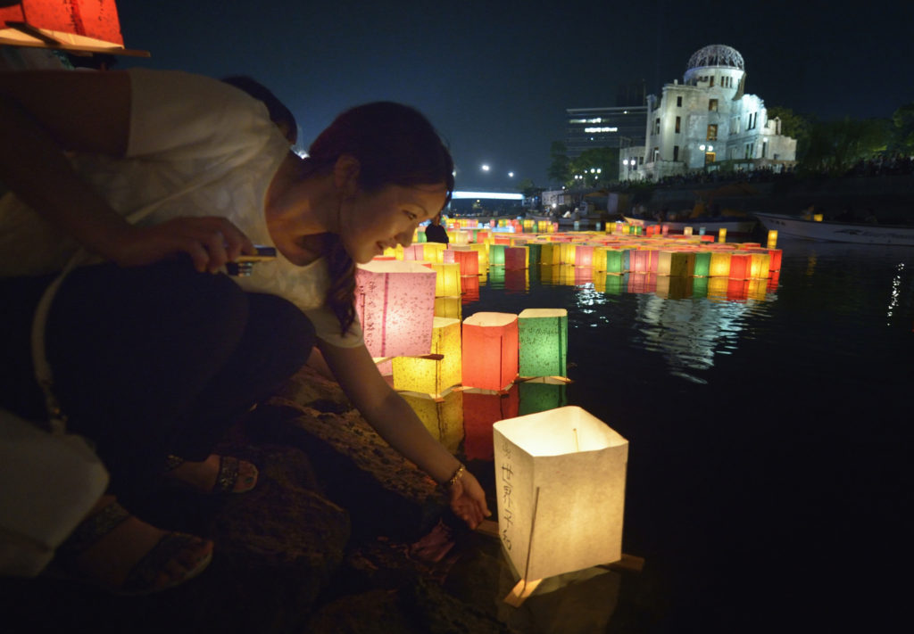 A woman sets a floating candle lantern on the river Aug. 6 in Hiroshima, Japan. The lanterns, thousands of which were launched on the 70th anniversary of the atomic bombing of the city, bear handmade messages and drawings, conveying each person's prayers for peace and comfort for the victims of the violence. In the background are the ruins of a building damaged by the bomb and now converted into a peace memorial. (CNS photo/Paul Jeffrey)