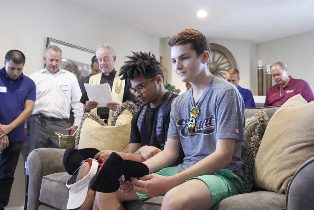 Alyisse and Julio, members of the Boys Hope Girls Hope residential program attend the opening of their newly remodeled home. Behind them, Jesuit Father Edward Reese leads those in attendance in prayer. (Ambria Hammel/CATHOLIC SUN)