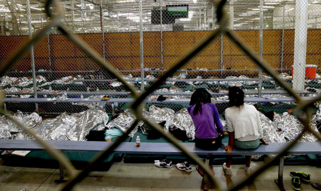 Two young girls watch a World Cup soccer match on a television from a holding area where hundreds of mostly Central American immigrant children are being processed and held at the U.S. Customs and Border Protection Nogales Placement Center in Nogales, Ariz., June 18, 2014. The federal agency provided media tours that day of two locations in Brownsville, Texas, and Nogales that have been central to processing at least 52,000 unaccompanied minors who have been detained in the U.S. this fiscal year. (Ross D. Franklin/CNS photo pool via Reuters)
