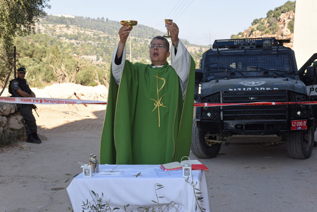 Father Aktham Hijazin of Beit Jalla, West Bank, celebrates Mass Sept. 3 in front of Israeli border police. Israel is uprooting the trees to make the way for the controversial separation barrier in the Cremisan Valley. (CNS photo/Debbie Hill)