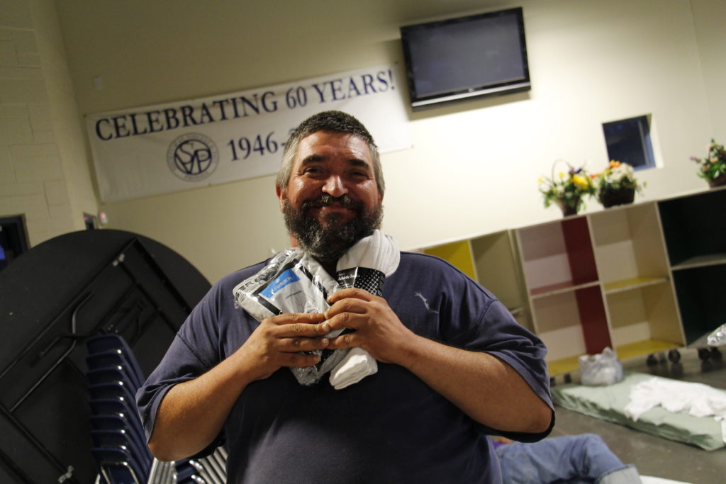 An overnight guest at St. Vincent de Paul's dining room on the Human Services Campus rejoices in his simple gifts of fresh socks and underwear. Staff and volunteers transform its dining facility nightly into makeshift dorms. (Ambria Hammel/CATHOLIC SUN)