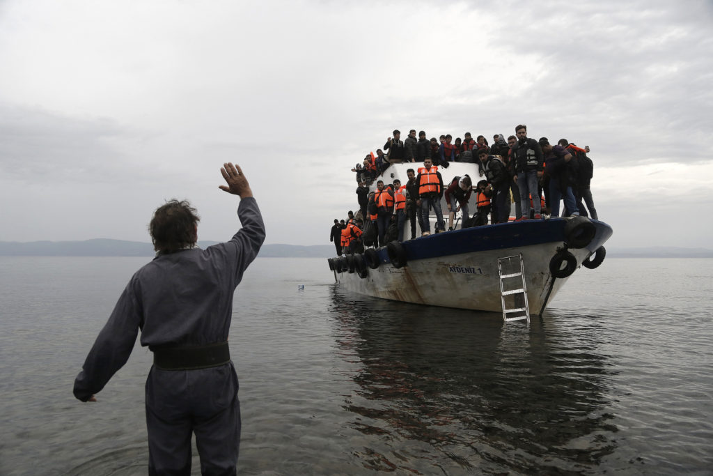 A resident waves to an overcrowded fishing boat carrying migrants after they arrived on the Greek island of Lesbos Oct. 11 after crossing the Aegean sea from Turkey. Greece is bracing for thousands more Syrian and other migrants to land on Lesbos and other key island crossings from Turkey, as those fleeing conflict remain undeterred by the worsening weather and colder autumn temperatures. (CNS photo/Yannis Kolesidis, EPA) 
