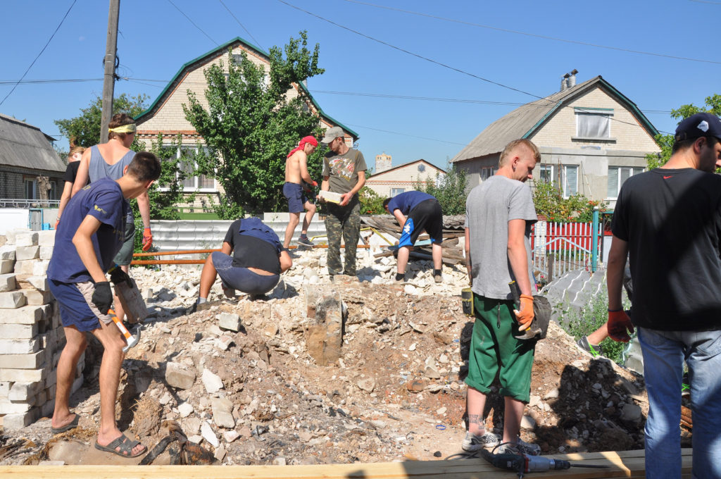 Volunteers from Lviv, Ukraine, clear debris to repair sewer and septic tank lines Aug. 5 in eastern Ukraine. The home was destroyed by three mortar shells during the war. (CNS photo/Maria Voronchuk) 