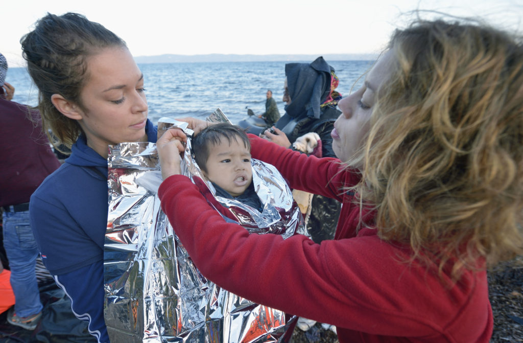 Volunteers wrap insulating material around a shivering refugee child on a beach near Molyvos, on the Greek island of Lesbos, Oct. 30. The child was on a boat full of refugees who paid huge sums to traffickers to travel from Lesbos to Turkey. (CNS photo/Paul Jeffrey)