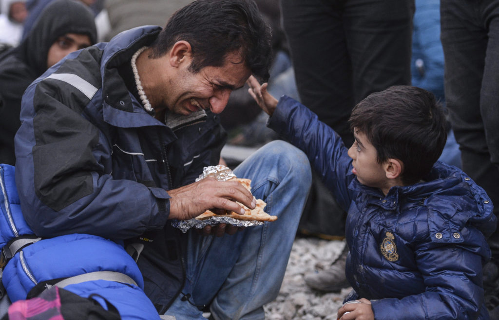 A boy touches his crying father during a Nov. 19 protest by angry migrants from Pakistan and Morocco who blocked a section of the Greece-Macedonia border after Macedonia began granting entry only to refugees from Syria, Iraq and Afghanistan. (CNS photo/Georgi Licovski, EPA)