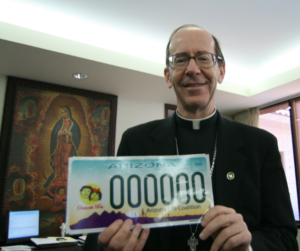 Bishop Thomas J. Olmsted holds a mock-up of the “Choose Life” Arizona license plate in this file photo. His car has displayed a similar plate since 2009 when the design became available through Arizona’s Motor Vehicle Division. Proceeds from the specialty plate fee support local pro-life programs. (File Photo/CATHOLIC SUN)