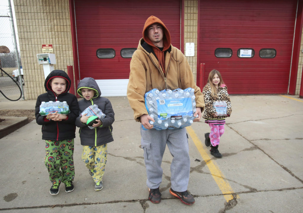 Flint resident Jerry Adkisson and his two children carry bottled water from a fire station in Michigan Feb. 7. (CNS photo/Rebecca Cook, Reuters) 