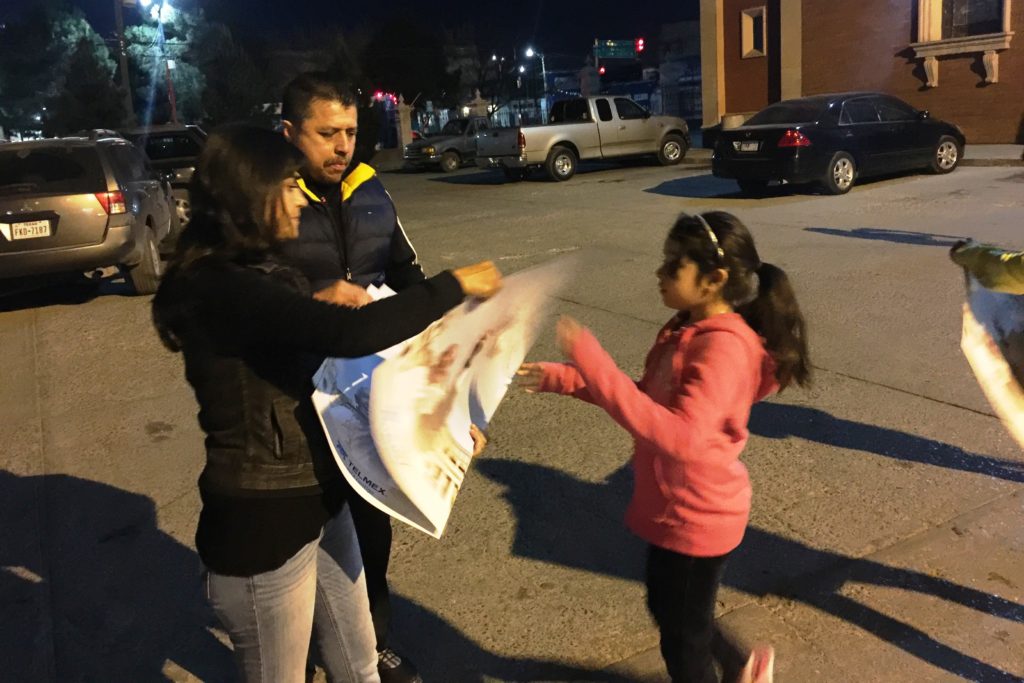 Lourdes Gutiérrez distributes a free commemorative poster of Pope Francis’ visit to Mexico to a young pilgrim in the San Lorenzo (St. Lawrence) Parish parking lot. (Tony Gutiérrrez/CATHOLIC SUN)