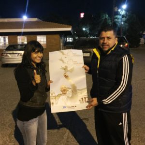 San Judás (St. Jude) parishioners Lourdes Gutiérrez and Carlos Torres hold a copy of a poster they were distributing for free to pilgrims Monday night. They belong to an unnamed group that wishes to show hospitality and mercy to the pilgrims. (Tony Gutiérrrez/CATHOLIC SUN)