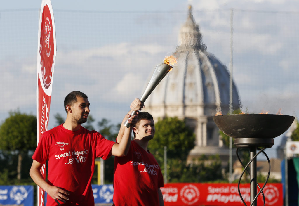 Salvatore Ruiu and Davide Paulis hold a torch during the opening ceremonies for the Special Olympics soccer tournament sponsored by the Knights of Columbus in Rome May 20. The tournament is being held to bring together players with and without intellectual disabilities as a model for how communities can include those with disabilities. The dome of St. Peter's Basilica is seen in the background. (CNS photo/Paul Haring)
