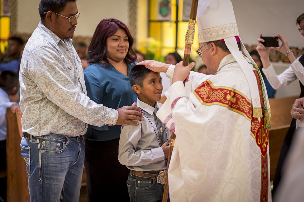 Auxiliary Bishop Eduardo A. Nevares lays his hands on Brian Allison, with his sponsors Samantha and Tyler Tashquinth standing behind him, during a Confirmation Mass at May 5 at St. Peter Mission in Bapchule. Waves of young Catholics are being confirmed throughout the Diocese of Phoenix with 31 more ceremonies scheduled this spring. (Billy Hardiman/CATHOLIC SUN)