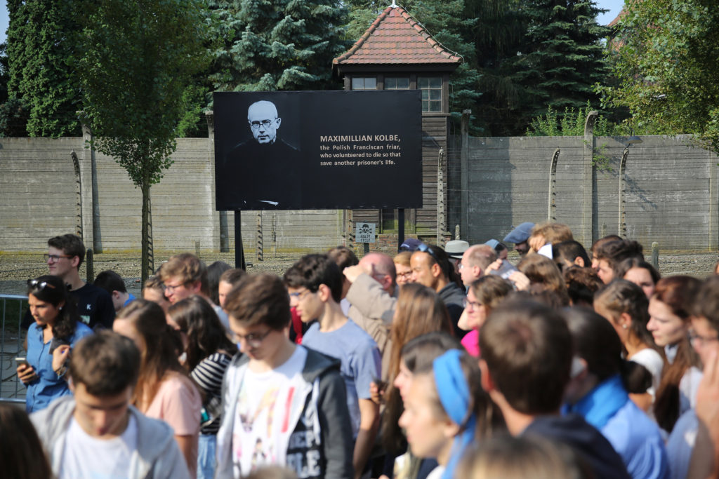 World Youth Day pilgrims and other visitors pause near an image of St. Maximilian Kolbe during a July 25 visit to the Auschwitz Nazi concentration camp in Oswiecim, Poland. St. Maximilian Kolbe took the place of a young father condemned to die at Auschwitz during World War II. (CNS photo/Bob Roller) 