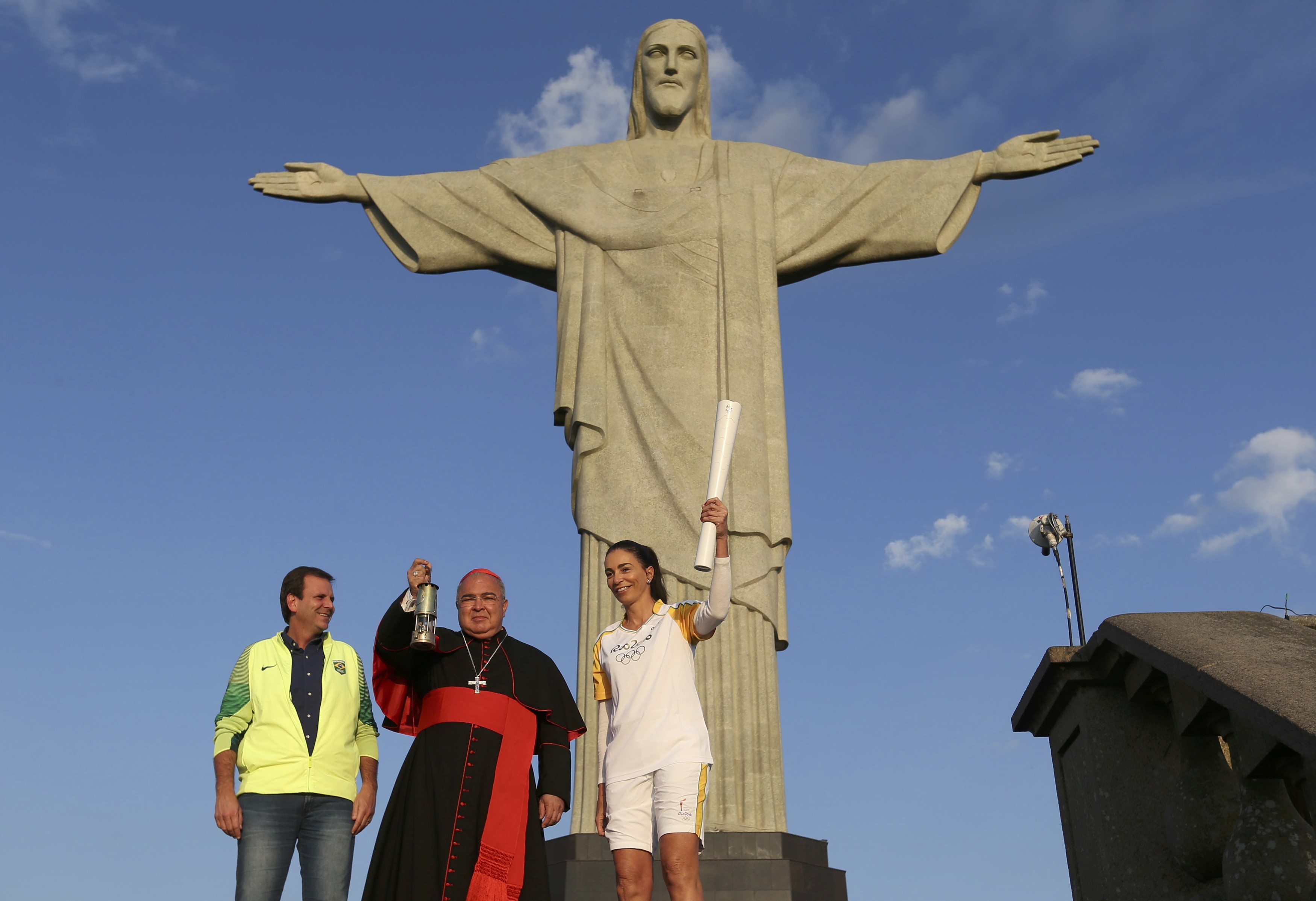 Cardinal Orani Tempesta of Rio de Janeiro holds the Olympic flame Aug. 5 as Rio Mayor Eduardo Paes and former Brazilian volleyball player Isabel Barroso look on in front of the Christ the Redeemer statue. (CNS photo/Pilar Olivares, Reuters)