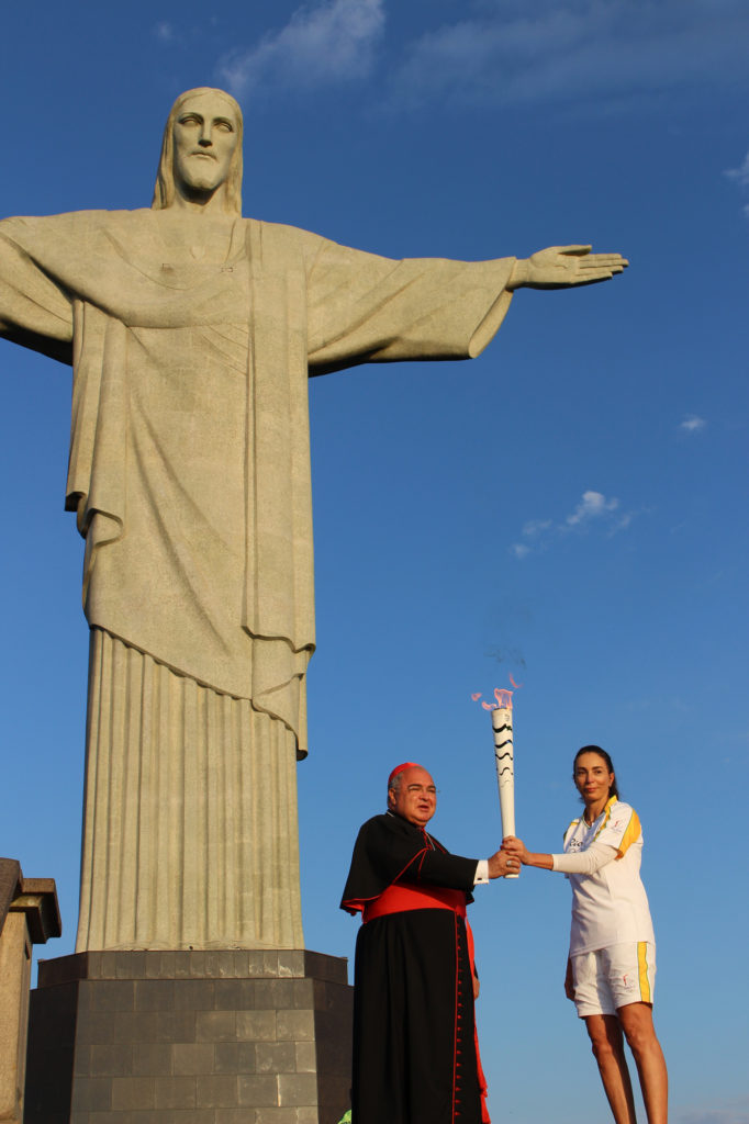 Cardinal Orani Tempesta of Rio de Janeiro and former Brazilian volleyball player Isabel Barroso hold the Olympic torch in front of the Christ the Redeemer statue in Rio de Janeiro Aug. 5. (CNS photo/Lise Alves)