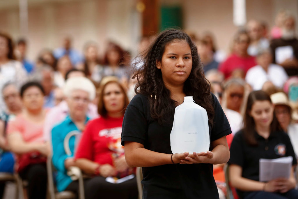 A young woman carries a gallon of water in the offertory during Mass at the international border in Nogales, Ariz., Oct. 23. The jug was presented as an offertory gift to symbolize all the people -- merciful Samaritans -- who have come to the aid of immigrants. (CNS photo/Nancy Wiechec) 