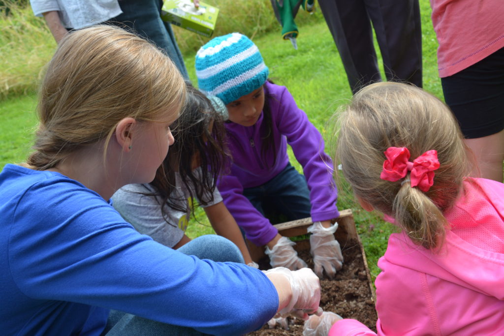 Ss. Simon and Jude students Embrey Saville, Emma Ballecer and Madison Ballecer, work alongside Lela Foster, a St. Theresa student, to plant seeds in Loreto sisters’ garden. (courtesy photo)