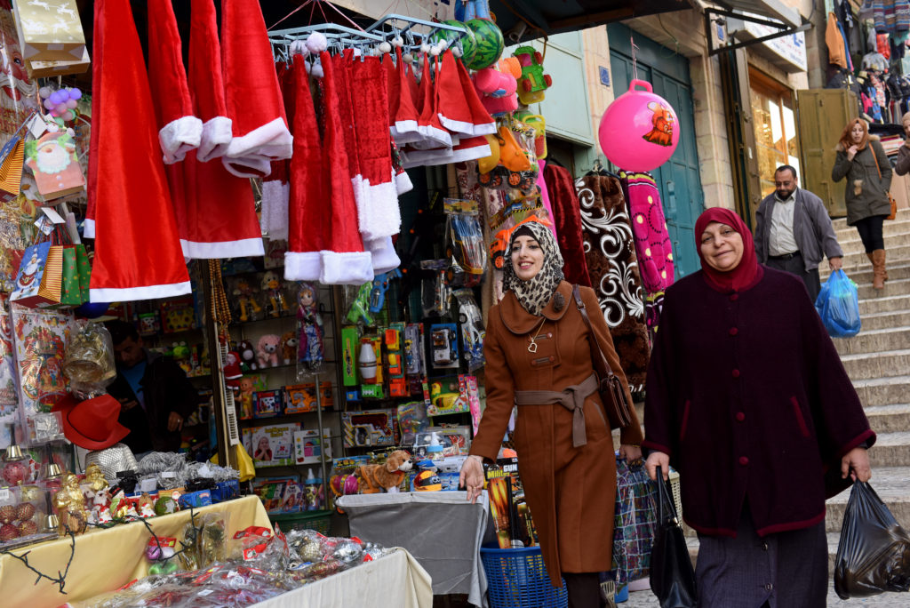 Palestinians walk past a shop selling Christmas decorations Dec. 5 near Manger Square in Bethlehem, West Bank. After two Christmas seasons in which the political reality had overtaken holiday cheer, people seem primed to finally feel some merriment in Bethlehem. (CNS photo/Debbie Hill) 